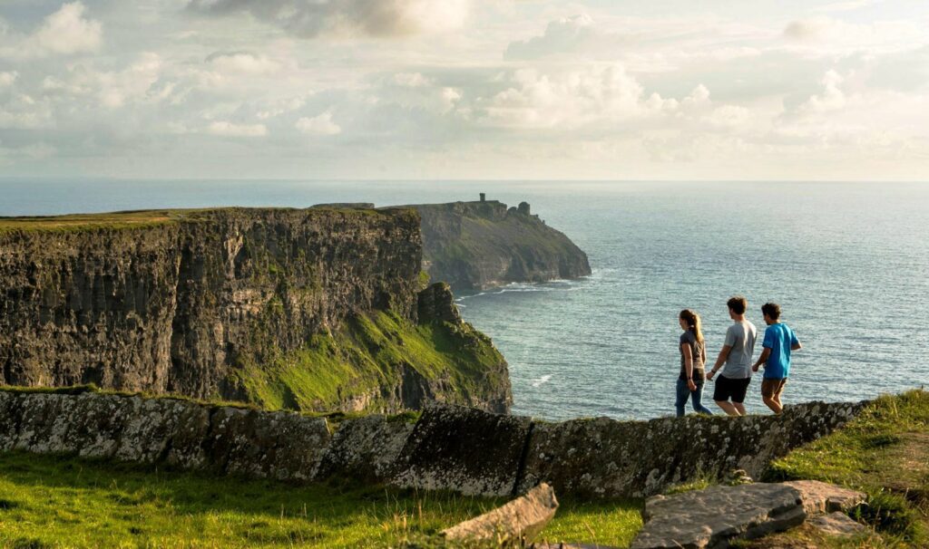 The cliffs run in tiered green layers down to the water, with a stone tower visible on the headland in the distance